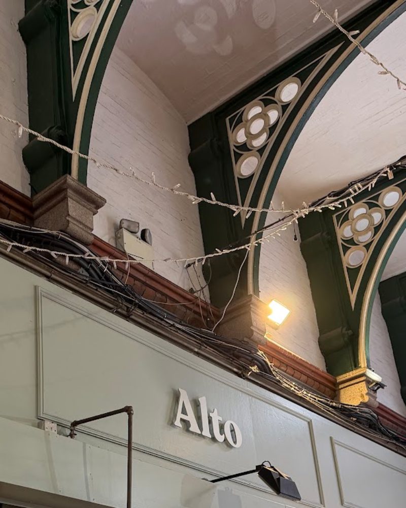Dark green Victorian cast-iron arches and gothic quatrefoils above Alto's sage-green sign in George's Street Arcade.